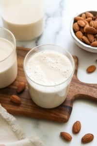 homemade almond milk on a cutting board with almonds on the counter.