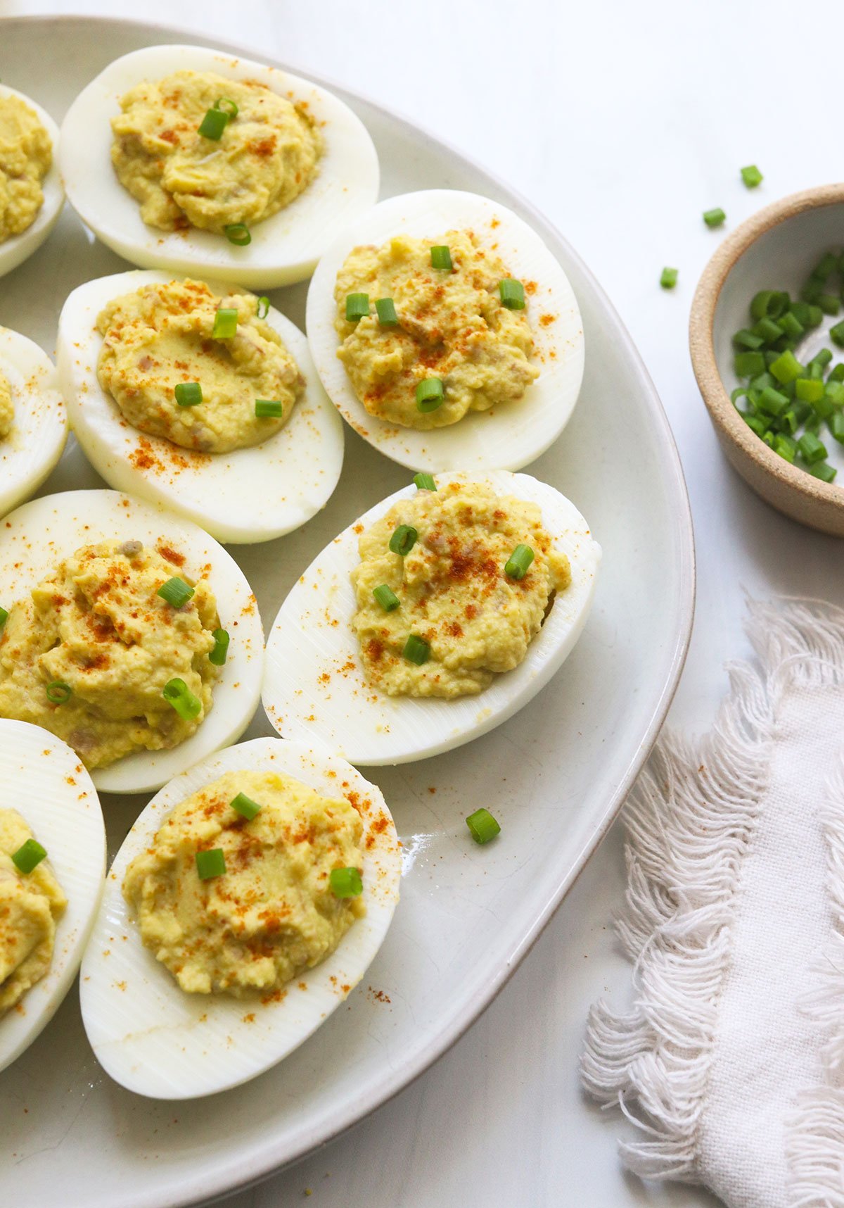 close up of avocado deviled eggs topped with chives and paprika.