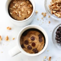 banana mug cake cooked in two white mugs with chocolate chips and walnuts on top.