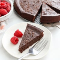 flourless chocolate cake slice on plate with raspberries.