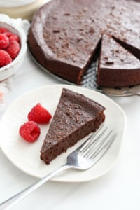 flourless chocolate cake slice on plate with raspberries.