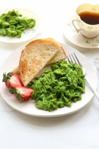 green eggs served on a plate with toast and strawberries.