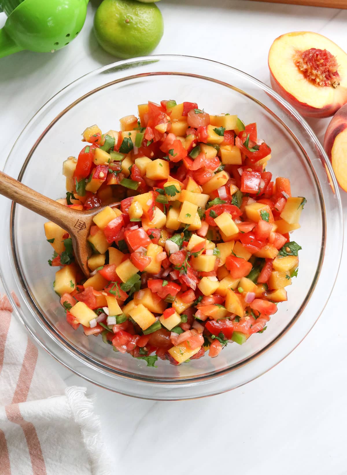 peach salsa served in a bowl next to limes and peaches.