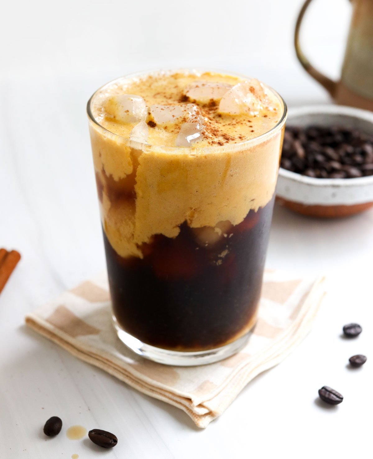 glass of iced coffee with pumpkin cream on top on white surface