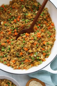 quinoa fried rice in white skillet with wooden spoon.