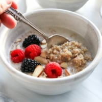 a spoon lifting up some quinoa porridge from a bowl with fruit.