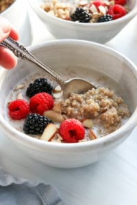 a spoon lifting up some quinoa porridge from a bowl with fruit.